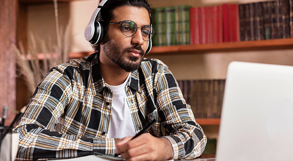 Blog on Keys to Choosing the Right Partner for Instructional Design: Image of a male student looking at PC screen and wearing headphones