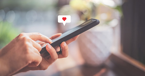 Image of a person texting on their phone with a heart icon over the screen.