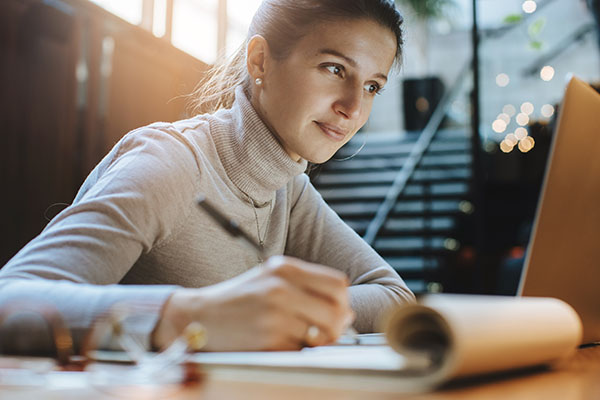 Blog on graduate enrollment trends: Professional women taking notes while watching an online course. 