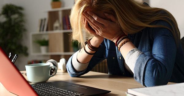 Blog on financing higher education: sad female student with her head in her hands in front of a laptop PC